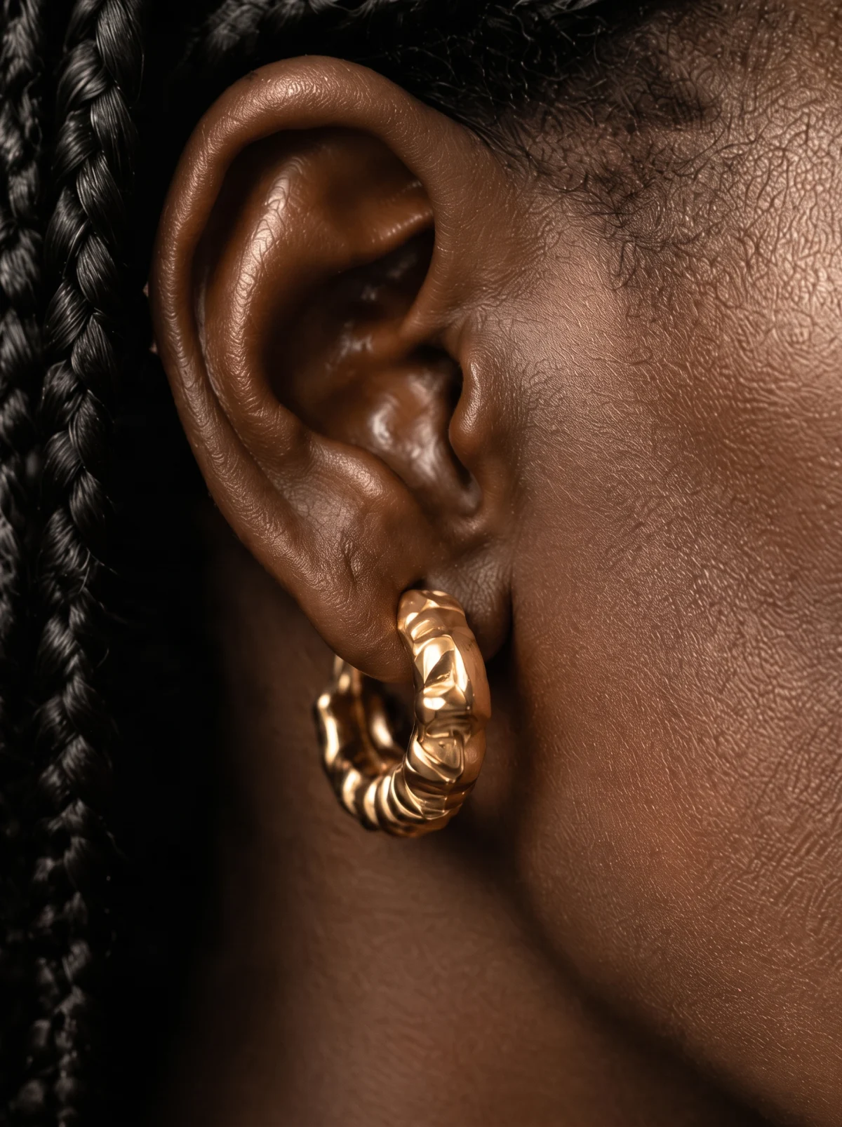 Close-up of a gold scalloped hoop earring on the ear, metal texture visible