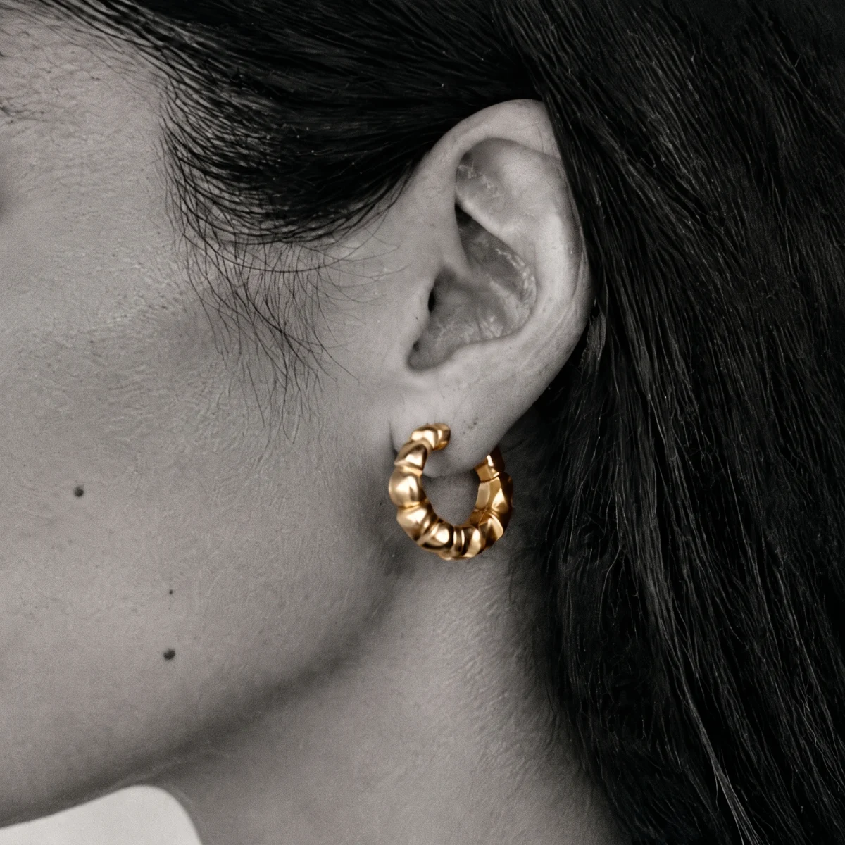 Gold scalloped hoop earring worn on the ear, soft side light, gray background