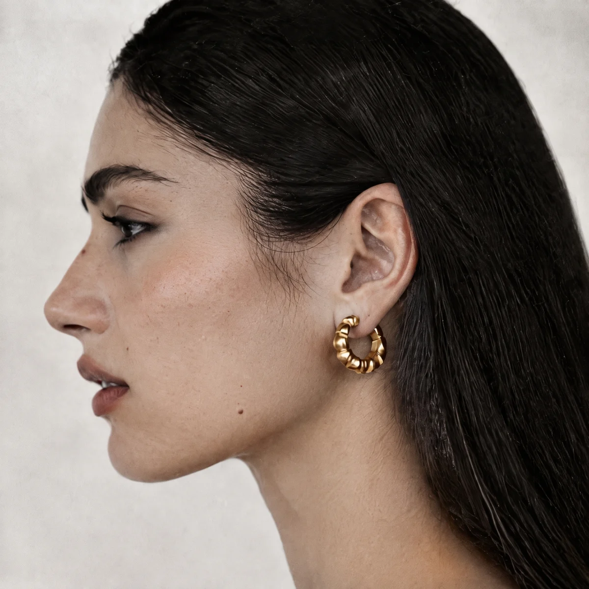 Woman in profile wearing a gold scalloped hoop earring, jawline in frame
