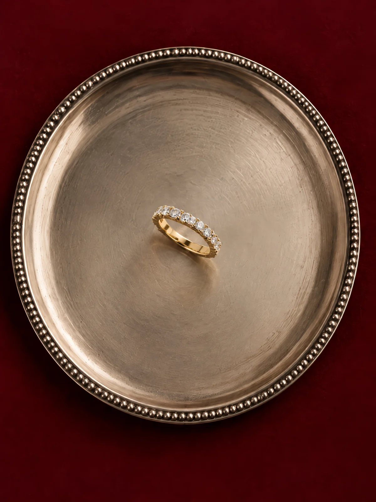 A gold diamond band on an antique silver tray with a beaded rim, over a deep red cloth
