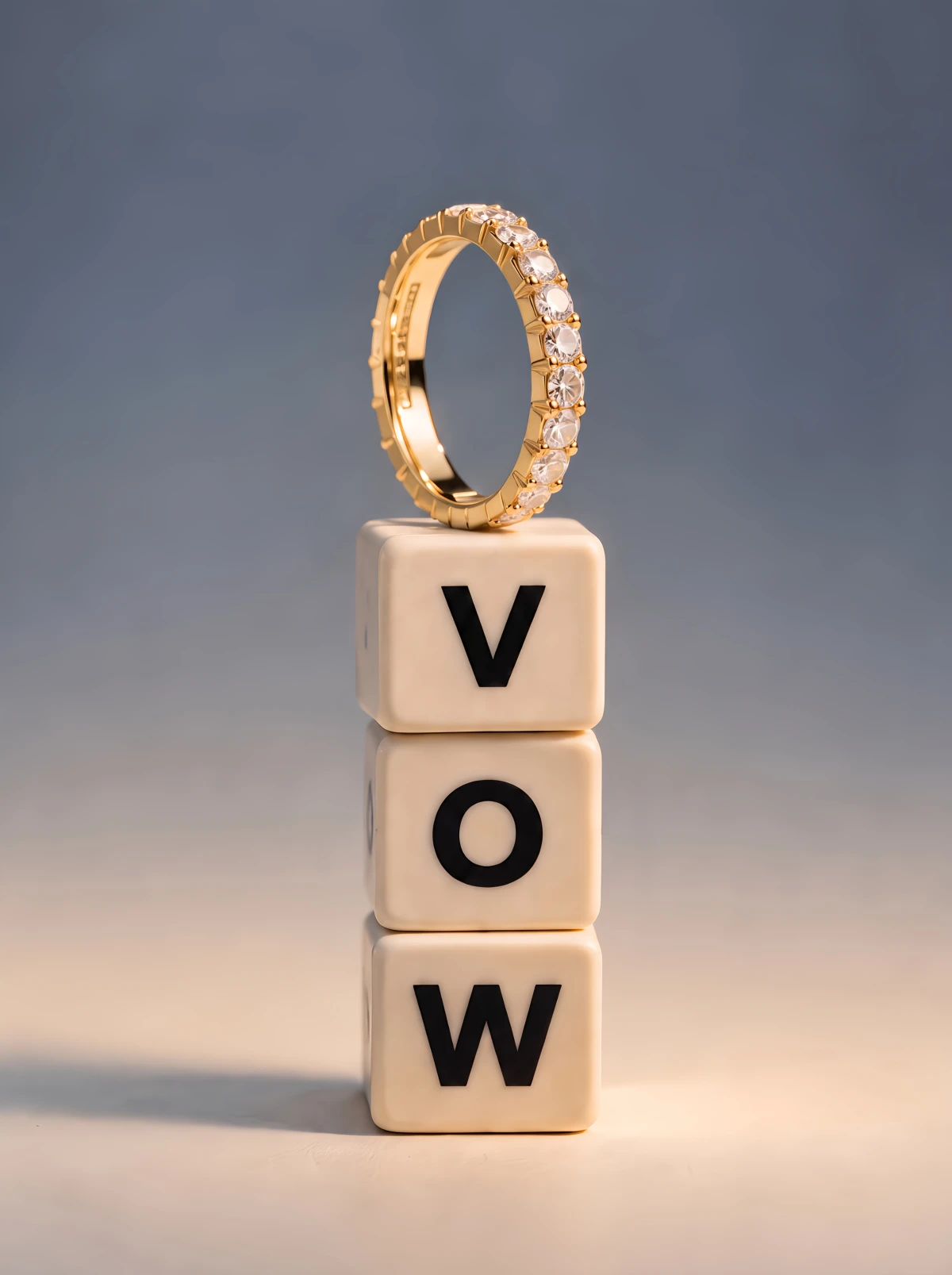 A gold diamond band balanced on three letter cubes stacked to spell VOW