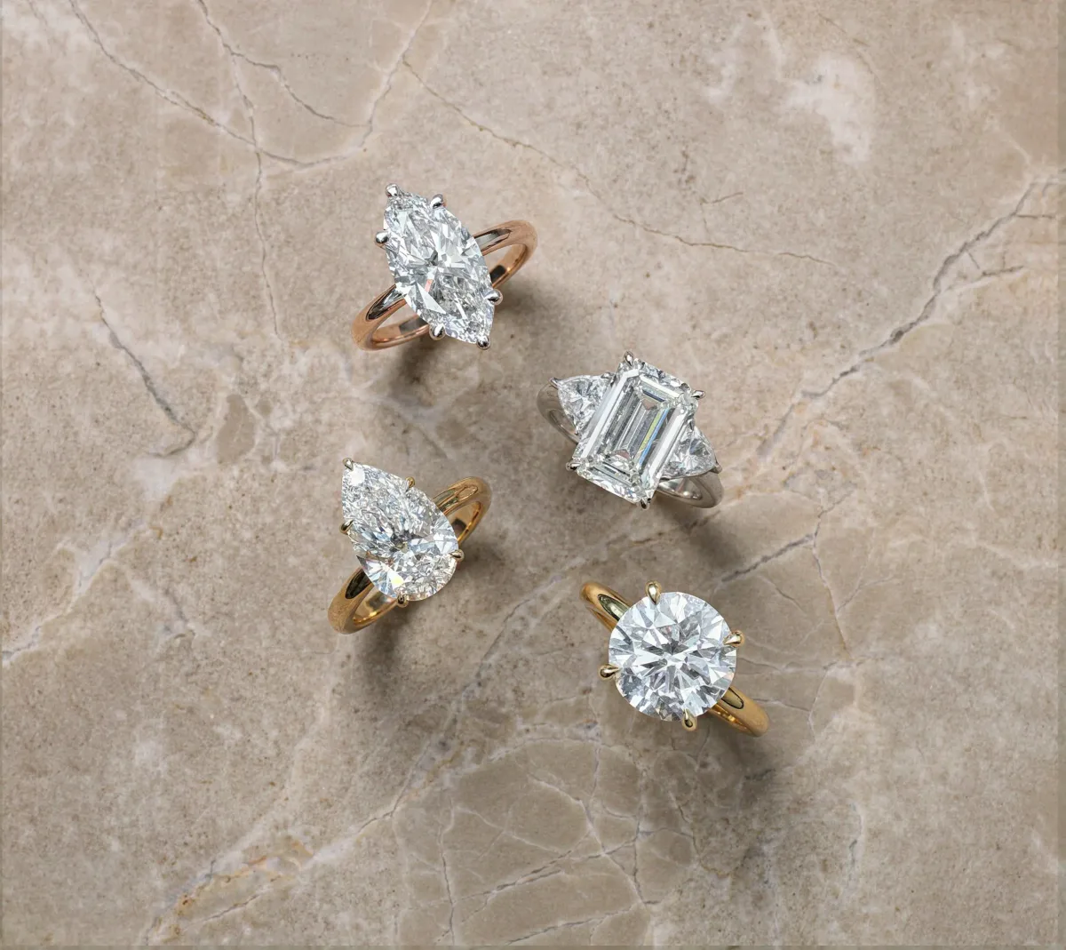 Flat lay jewelry photography: four diamond solitaire rings in different cuts on a beige stone surface