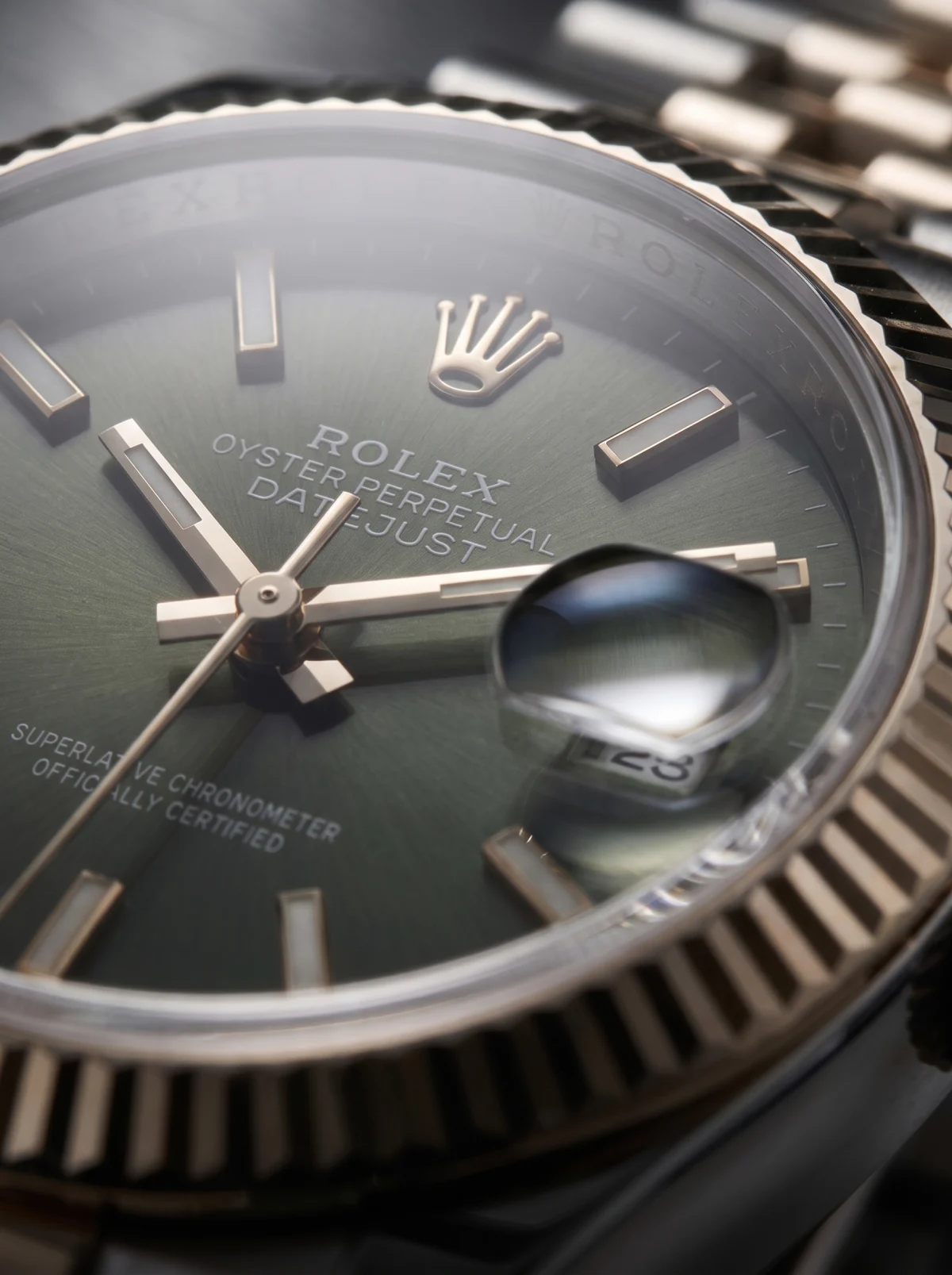 Close-up of a green watch dial: applied indices, the hands, the date under its magnifier and a fluted bezel