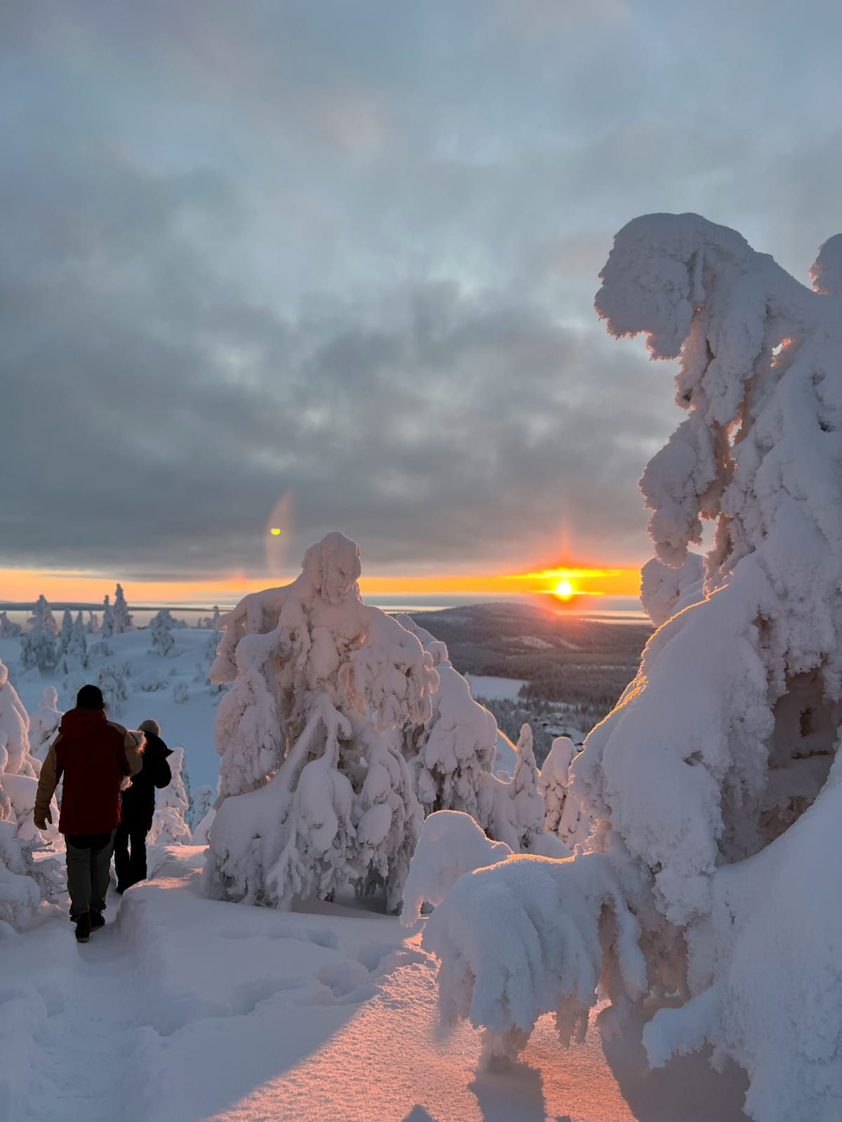 Two walkers on a snowy fell top near Levi as a low February sun breaks through