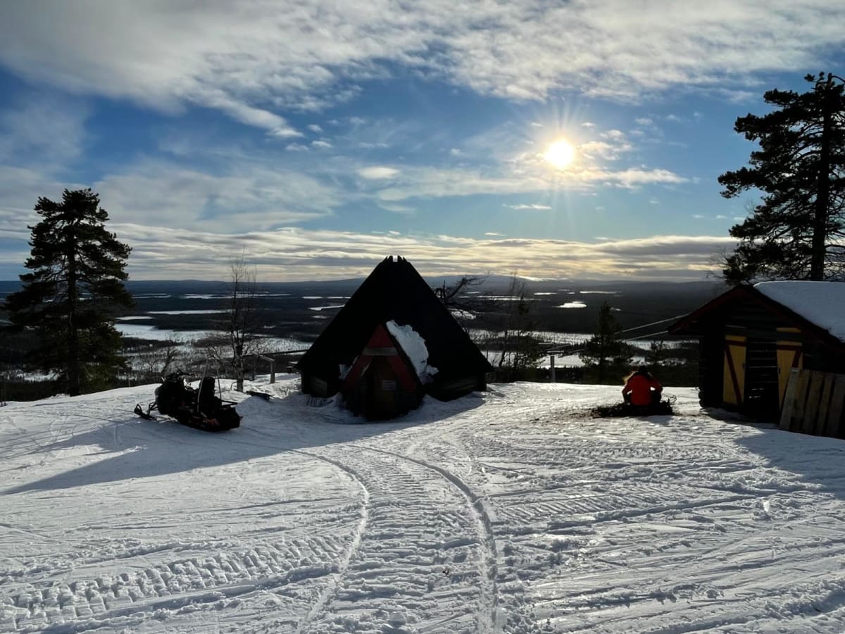 Snowmobiles parked beside a wooden kota on a snowy fell above Levi in bright March sun