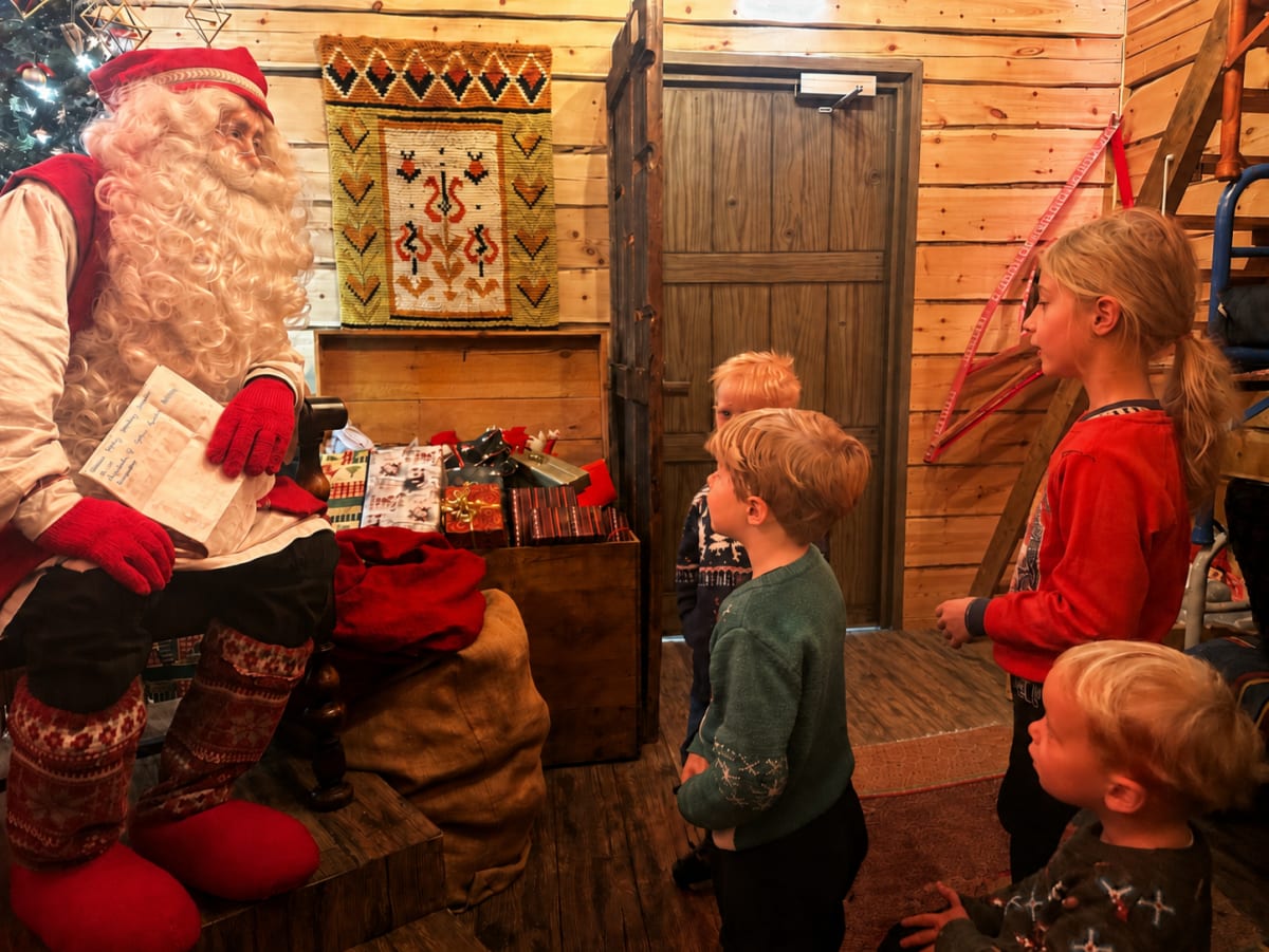 Children gathered around Santa as he reads a letter in his wooden cabin in Lapland