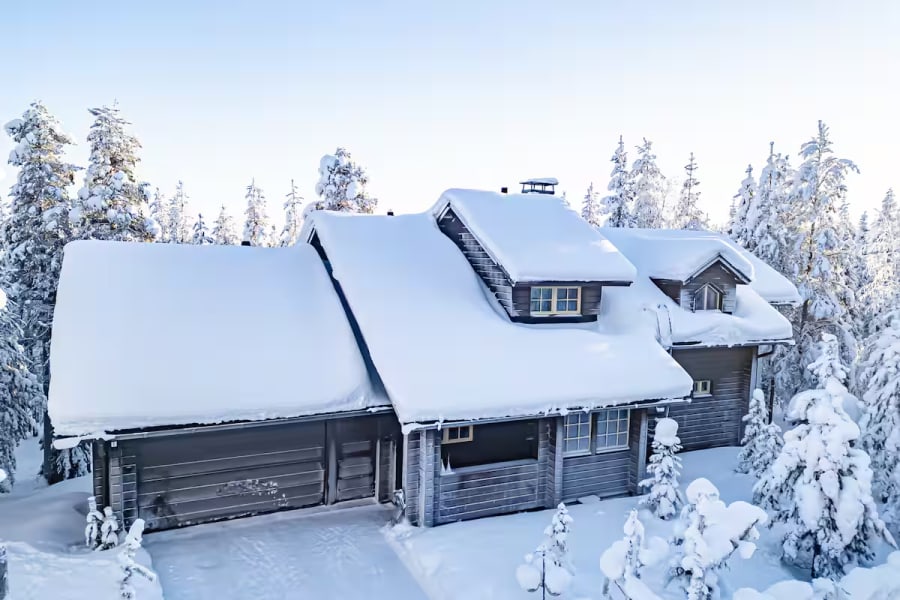 A snow-covered log cabin among pine trees in Levi
