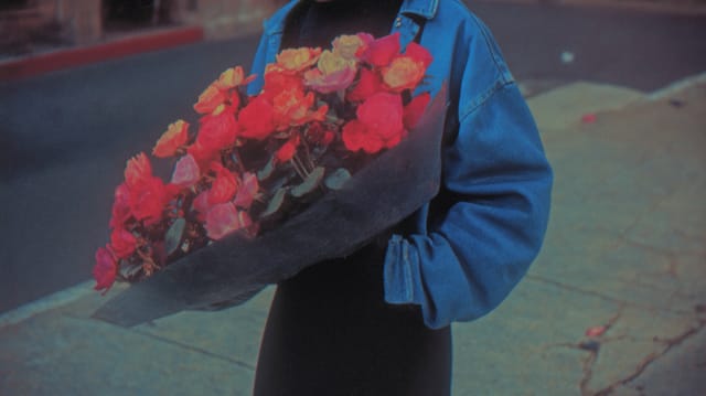 Person in a denim jacket holding a large bouquet of red flowers on a street