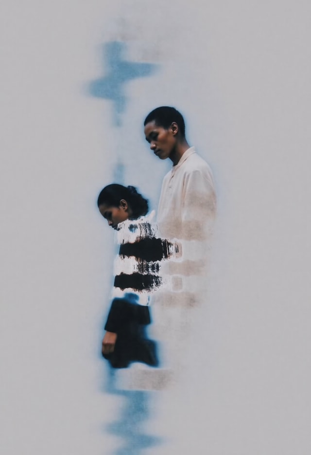 Two figures in patterned clothes against a pale background with blue ink-like streaks