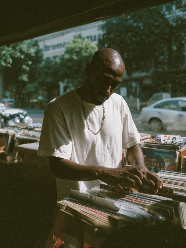 Man in a white t-shirt flipping through records at an outdoor market stall