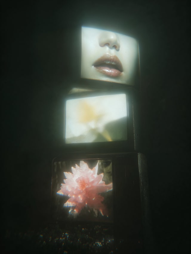 Three stacked televisions in the dark showing lips, a flower and a pink lotus