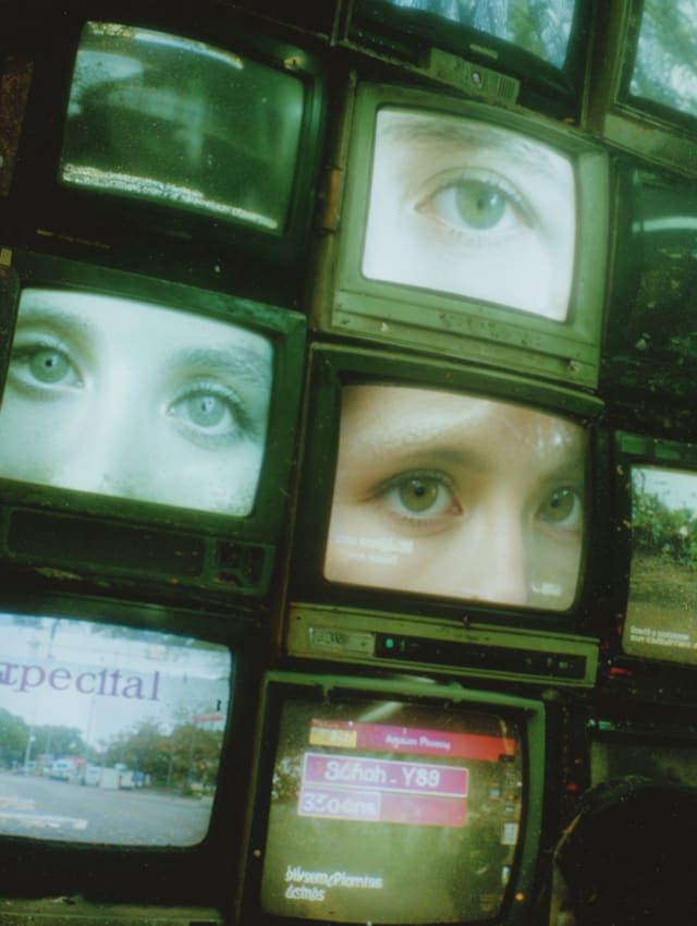 Wall of green-tinted television screens showing close-ups of eyes