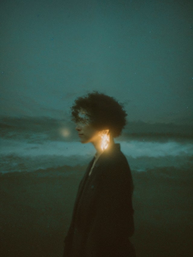 Curly-haired person from behind the shoulder at dusk on a beach with a small glowing light