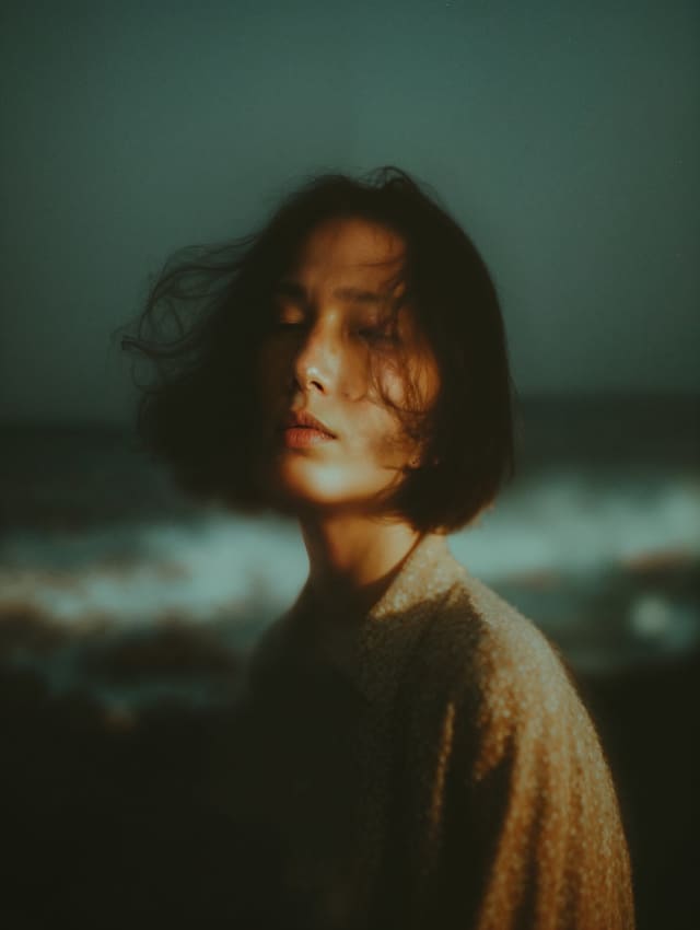 Portrait of a person with a bob haircut, eyes closed, wind in the hair, moody sea in the background