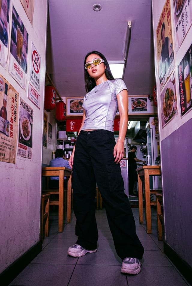 Woman in sunglasses and a white top standing in a narrow purple-lit restaurant hallway