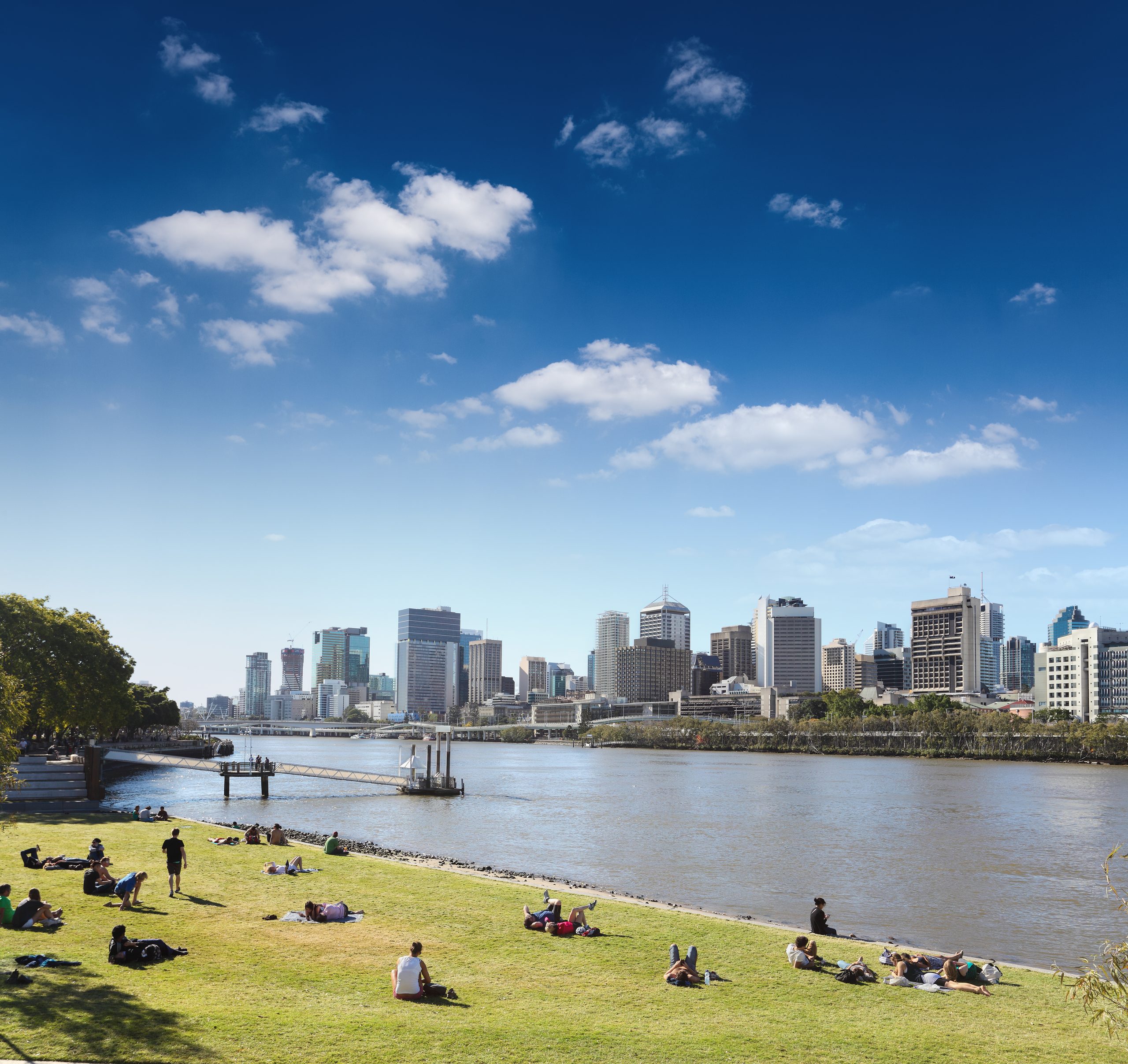 People relaxing on the South Bank parklands lawn with the Brisbane skyline behind