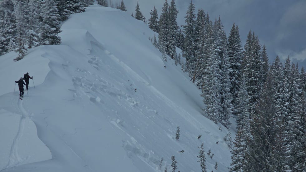 Backcountry skiers climb a ridge beside a large avalanche crown and debris on a steep slope near Marble Peak.