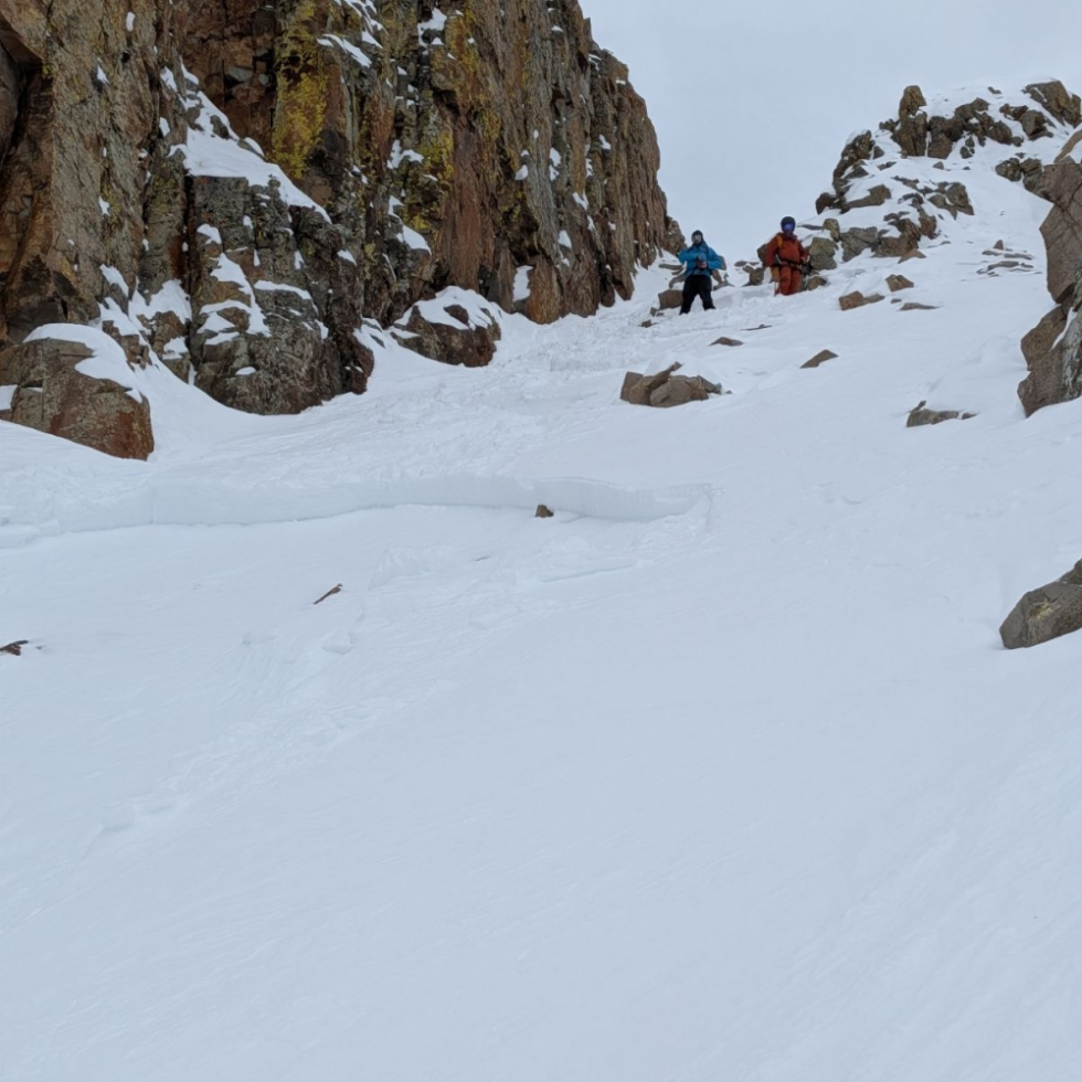 Two backcountry skiers descend a steep, rocky couloir in the San Juan Mountains above a small loose avalanche pocket that ran partway down the slope.