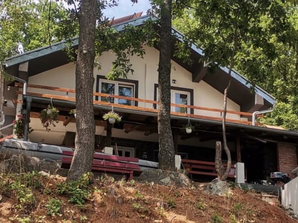 Spoljašnjost apartmana okružena stablima, drvena terasa sa cvećem