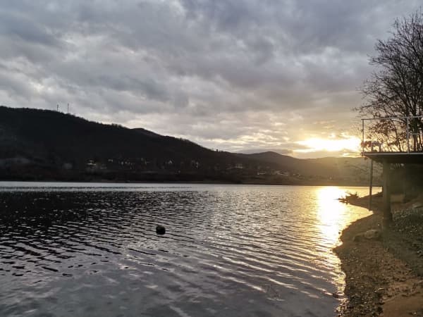 Zalazak sunca nad Bovanskim jezerom sa odrazom na mirnoj vodi i oblačnim nebom