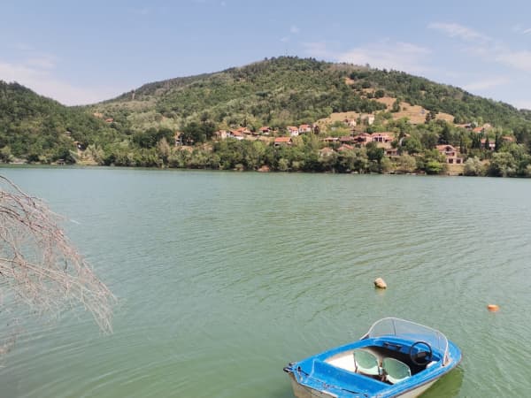 Plavi čamac usidren na jezeru, pošumljeno brdo sa selom u pozadini