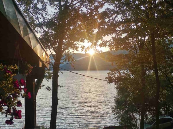 Zalazak sunca nad jezerom viđen sa terase, kroz drveće i cveće