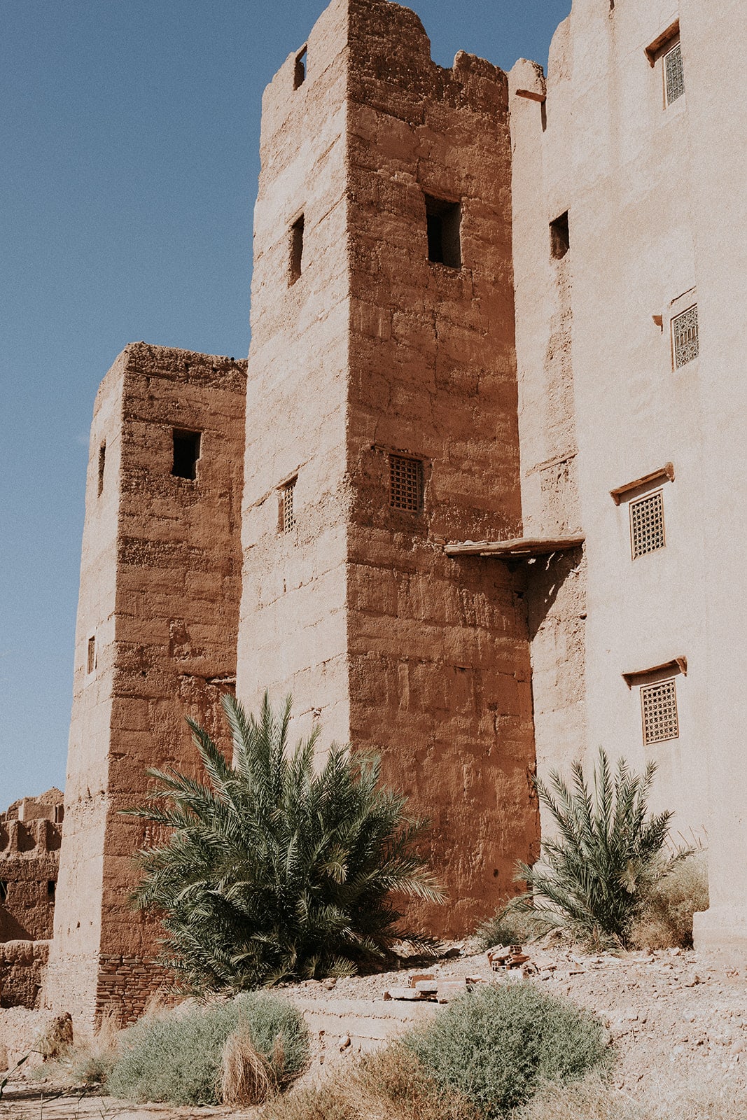 A bright sunlit pisé kasbah wall photographed against a clear sky, the warm earth tones showing the horizontal lift lines from the original construction forms, photorealistic editorial photography in the Architectural Digest register, no people, considered architectural composition, premium publication aesthetic, soft directional natural light, 16:9