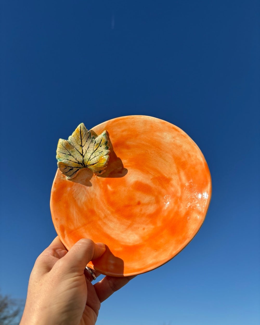 Ceramic plate with warm orange swirl glaze and a small decorative leaf attached to the rim, 18cm