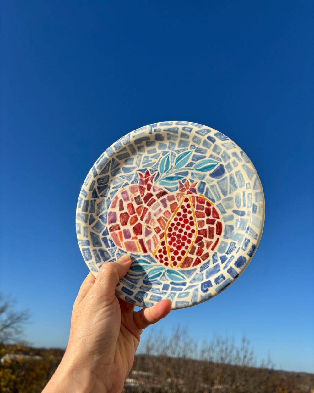 Ceramic plate with mosaic-style pomegranate design in rich red against a blue tile-effect background, 20cm
