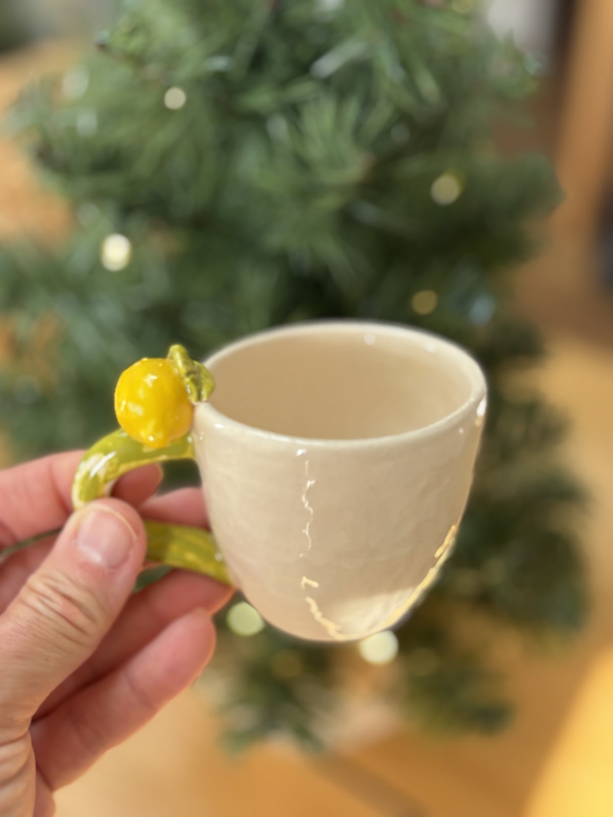 Handmade lemon espresso cup held in front of a softly lit Christmas tree