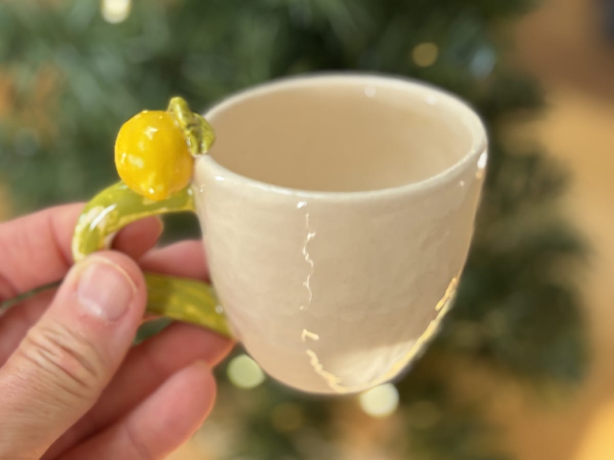 Handmade lemon espresso cup held in front of a softly lit Christmas tree