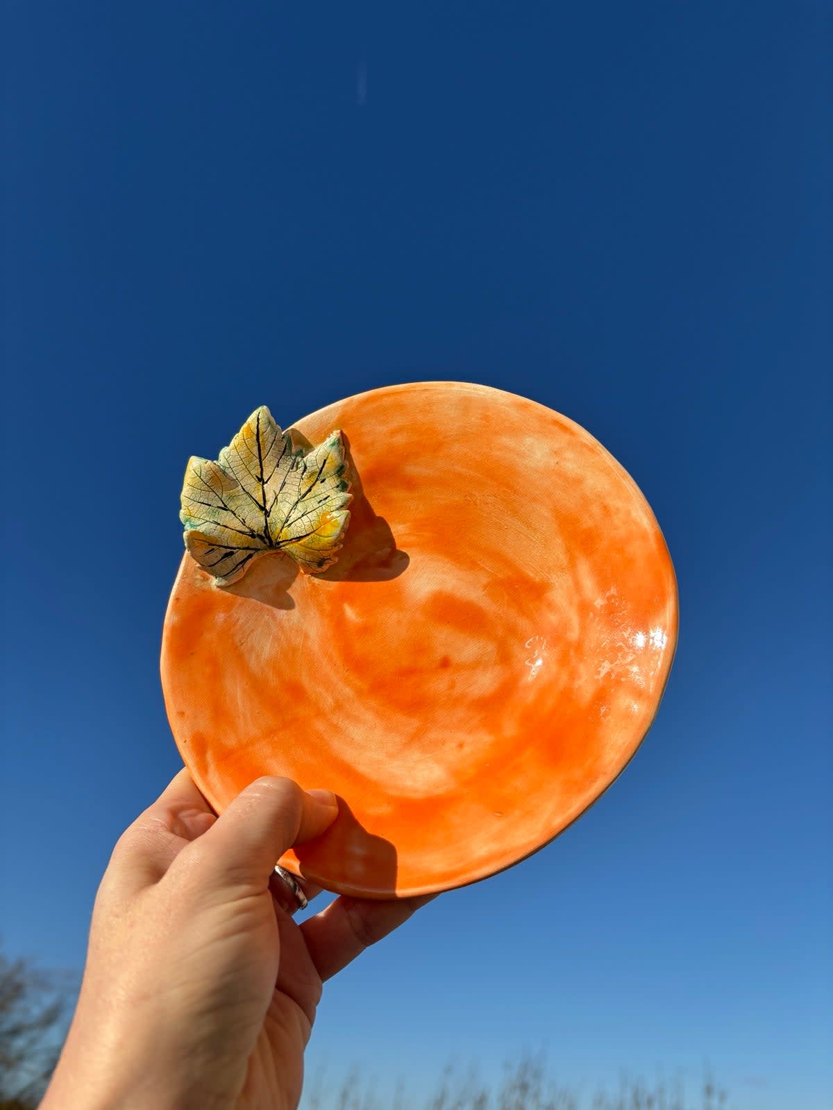 Ceramic plate with warm orange swirl glaze and a small decorative leaf attached to the rim, 18cm