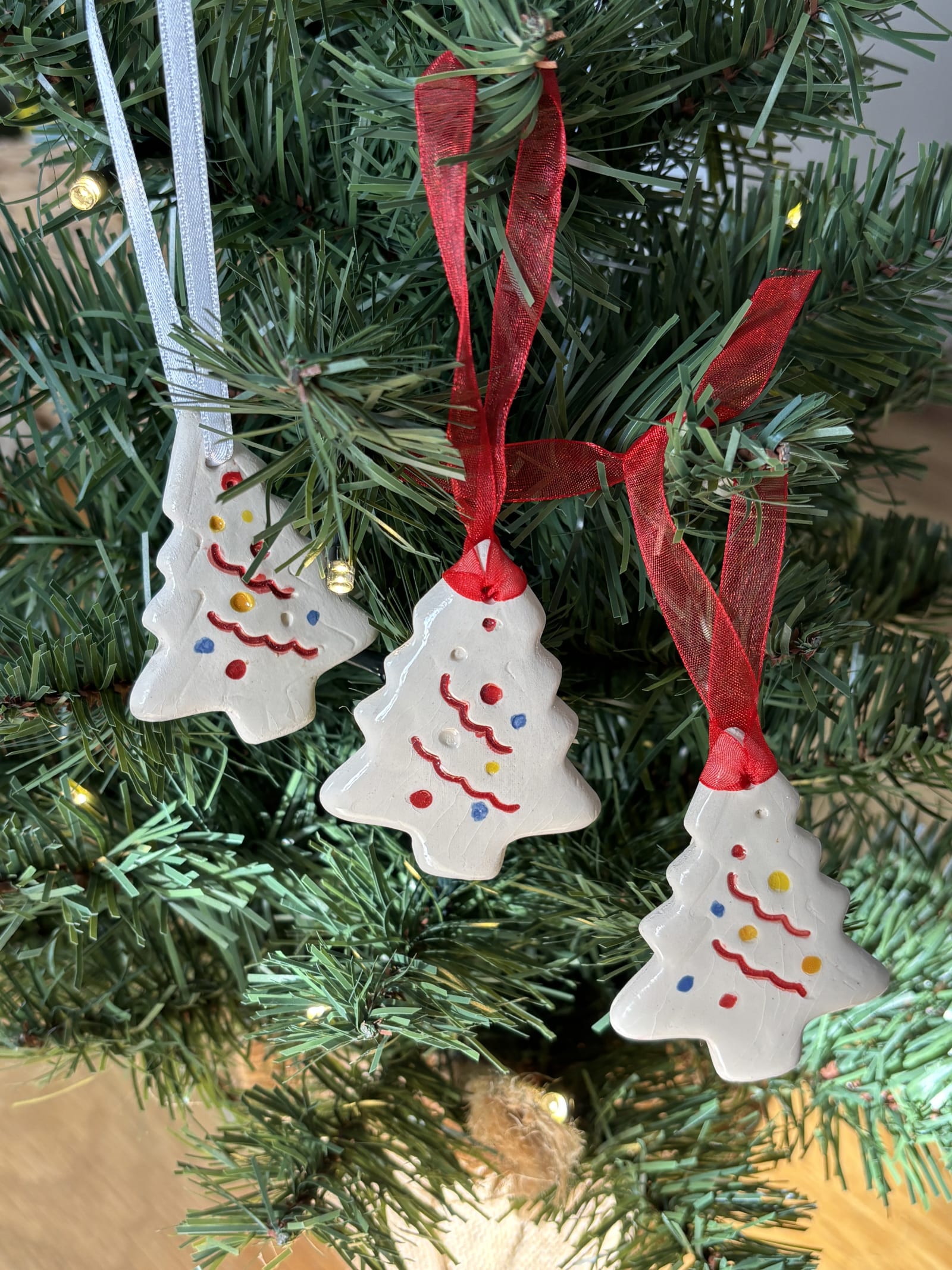 Set of three handmade ceramic Christmas tree ornaments with red ribbon hanging on a Christmas tree