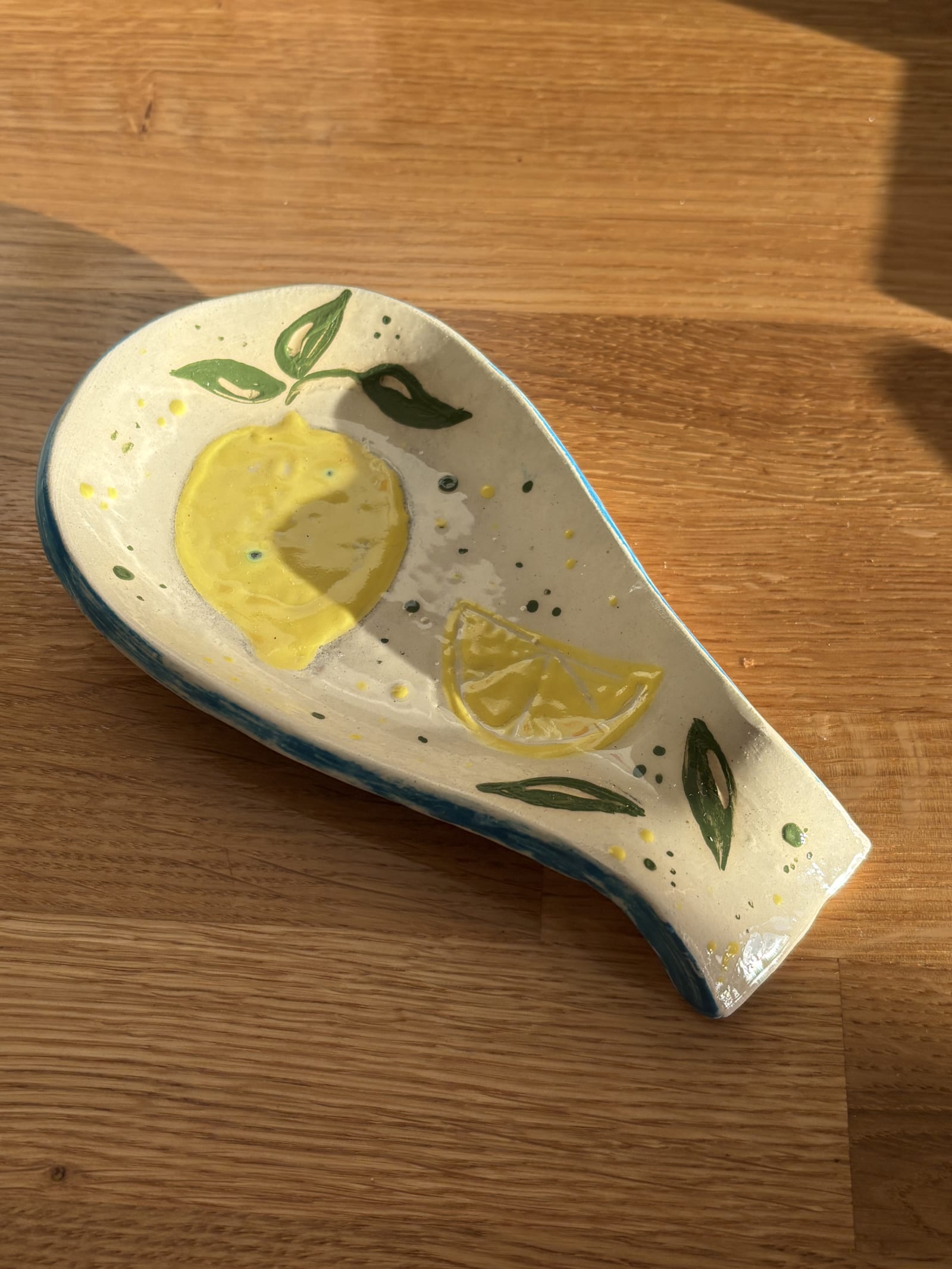 Handmade ceramic lemon spoon rest with hand-painted yellow lemons and green leaves. A colourful pottery kitchen accessory and unique handmade gift.