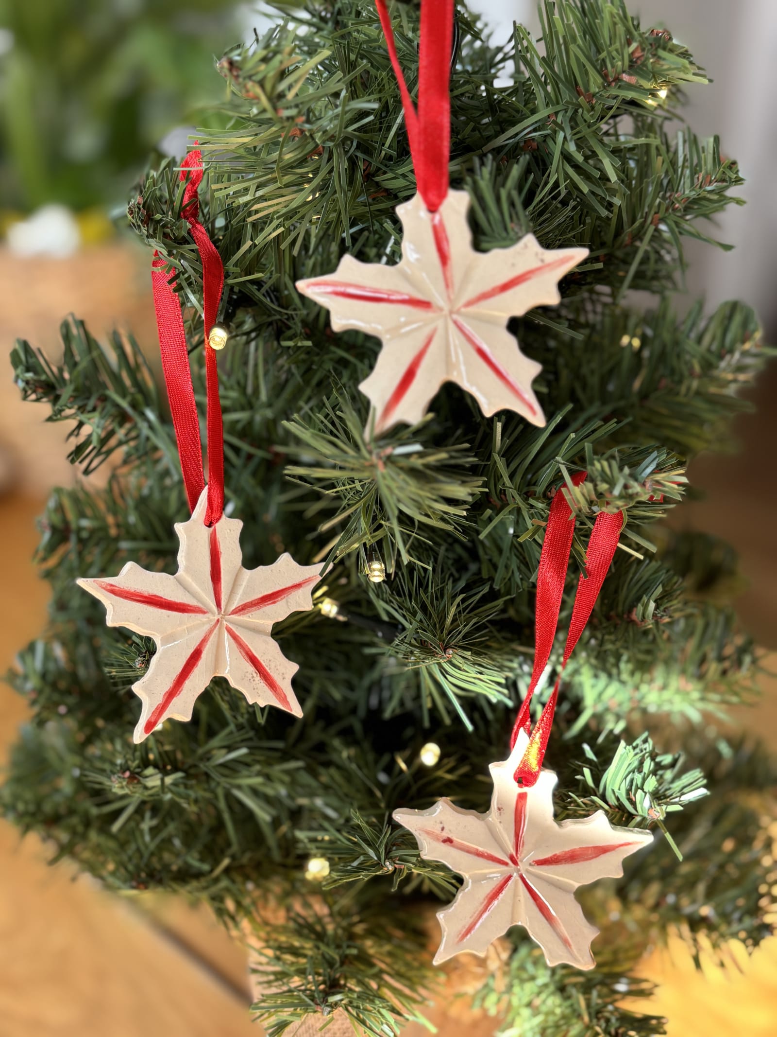 Set of three handmade ceramic Christmas star ornaments with red ribbon on Christmas tree