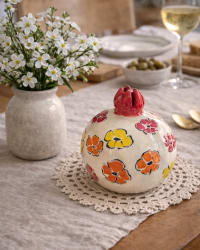 Ceramic pomegranate sculpture with hand-painted flowers in soft pastel tones on a rounded form