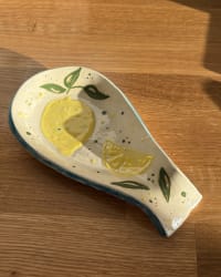 Handmade ceramic lemon spoon rest with hand-painted yellow lemons and green leaves. A colourful pottery kitchen accessory and unique handmade gift.