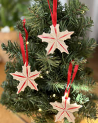 Set of three handmade ceramic Christmas star ornaments with red ribbon on Christmas tree