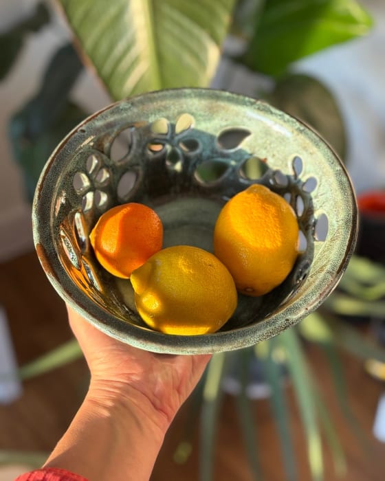 Deep turquoise ceramic fruit bowl with hand-cut floral openwork design showing light through the pattern