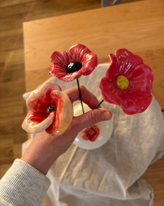 Three handmade ceramic flowers in rich red and coral tones on green metal stems, styled as a bouquet