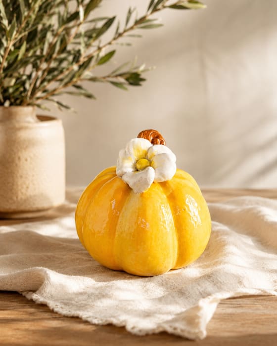 Handmade ceramic pumpkin with golden-yellow glaze and a white sculpted flower on top, placed on a linen cloth