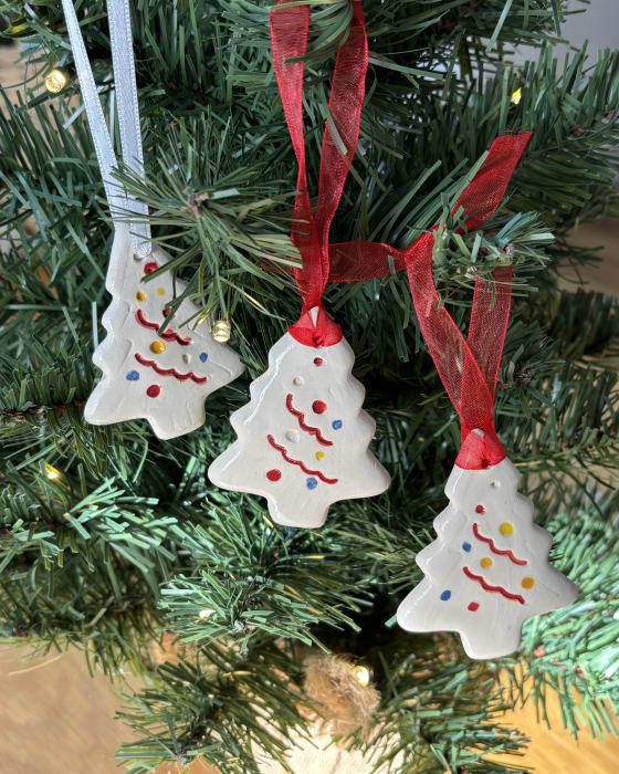 Set of three handmade ceramic Christmas tree ornaments with red ribbon hanging on a Christmas tree