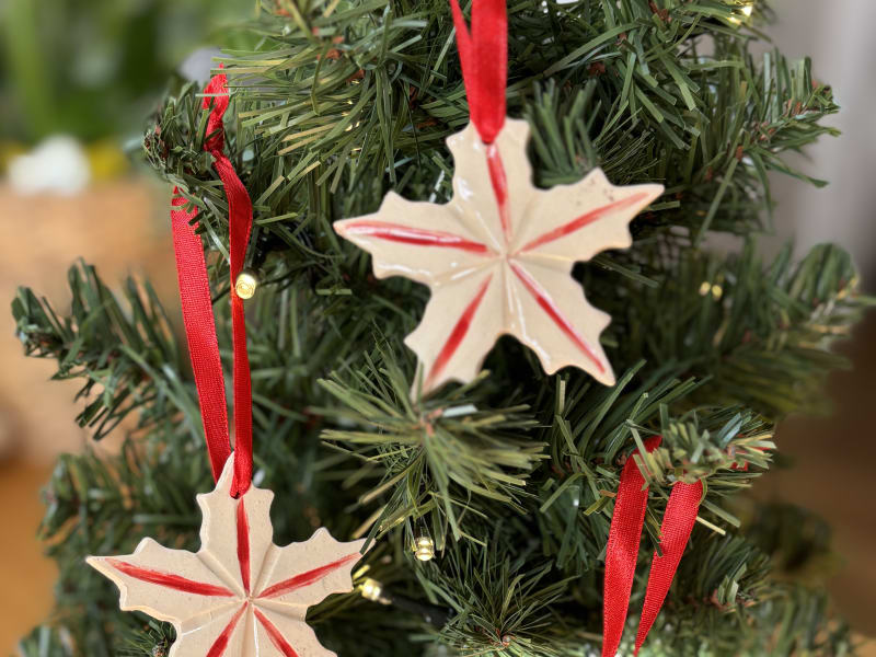 Set of three handmade ceramic Christmas star ornaments with red ribbon on a Christmas tree