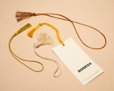 White bookmark with a variety of gold tassels surrounding it.