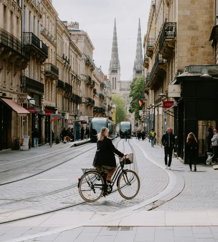 Photo d'une femme faisant du vélo le long de la rue Vital Carles à Bordeaux avec au loin la Cathédrale Saint-André de Bordeaux
