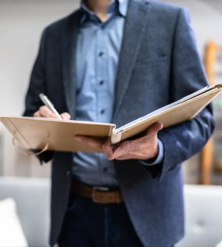 Un homme tenant un cahier sur lequel il note s'il y a des erreurs, ou non, qui on était commissent lors de l'achat d'un bien neuf.