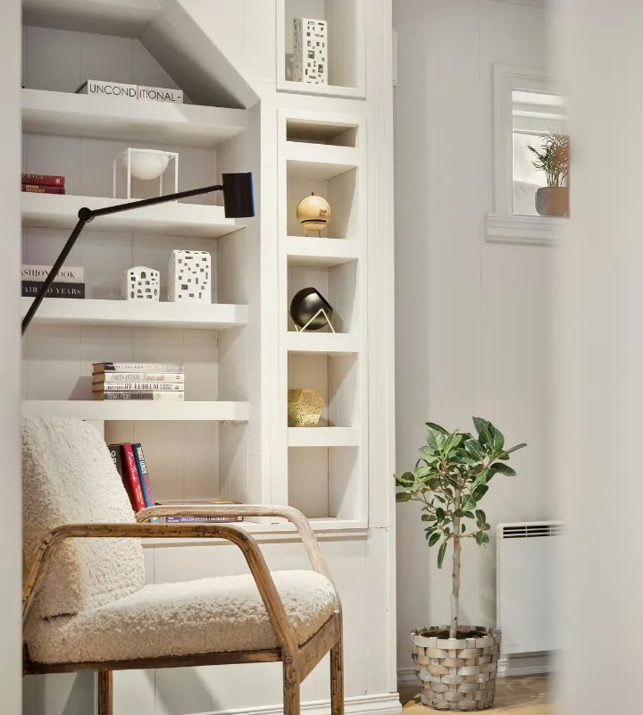 Intérieur blanc d'un appartement avec une chaise en premier plan, une plante sur le côté droit et des décorations