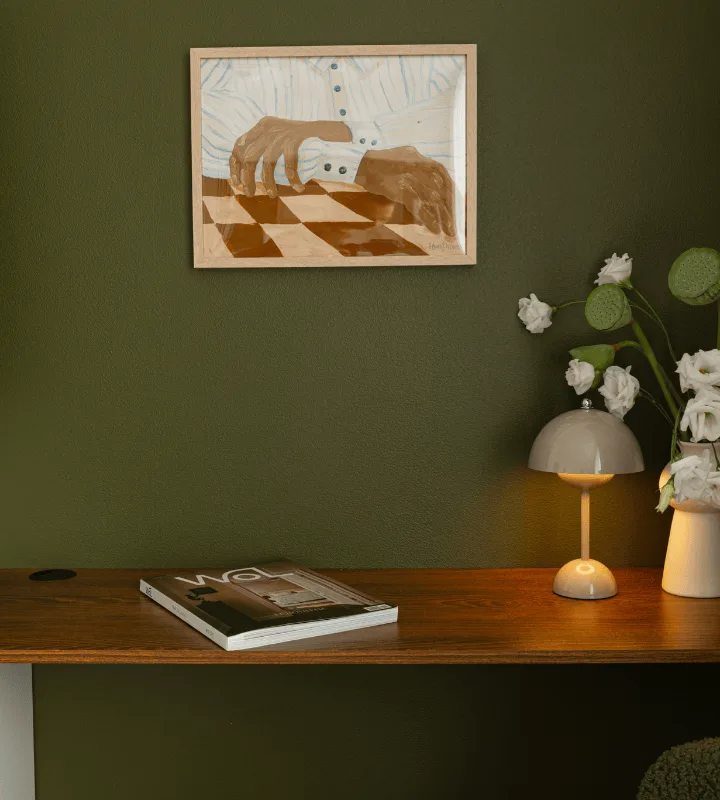 Une table en bois avec un journal et une lampe. Le mur du fond est vert foncé.