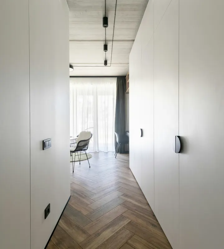 Couloir avec un plancher en bois et des murs blancs menant vers une chambre illuminé depuis la lumière naturelle provenant des fenêtres