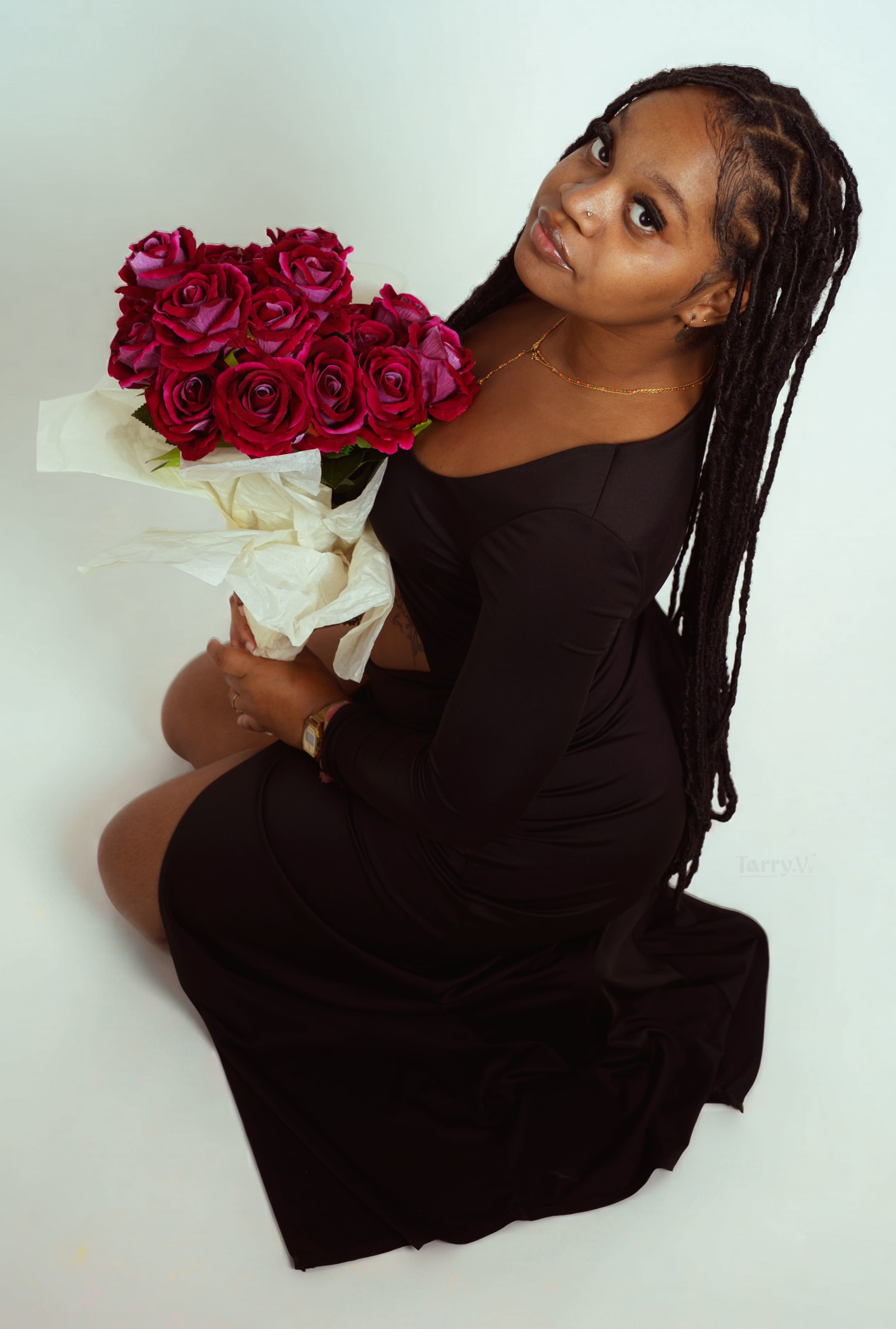 Loana assise au sol en robe noire, le bouquet de roses rouges leve a hauteur du visage